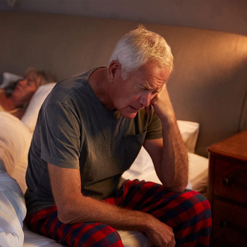 A man sitting on the edge of his bed, deep in thought