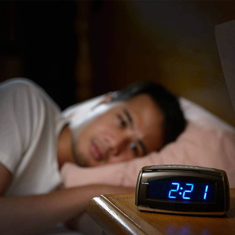 A man lying awake in bed at night next to his alarm clock